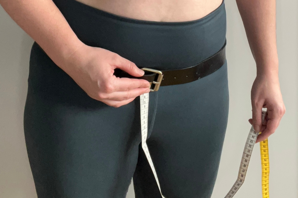 A photo of a model holding a measuring tape against the buckle of a belt sitting low on their hips
