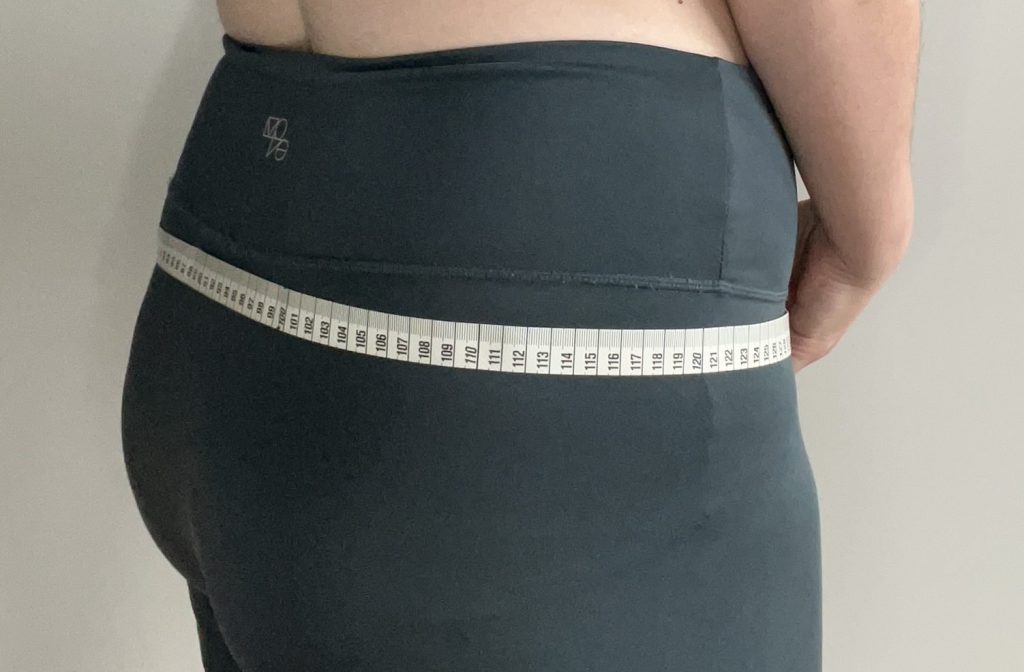 A close up photograph of the back and side of their hips. A white tape measure is wrapped around their hips.